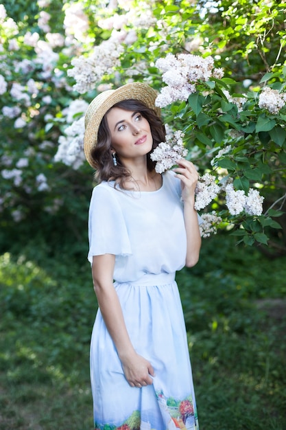 Portrait of a beautiful girl in a straw hat in a lilac garden