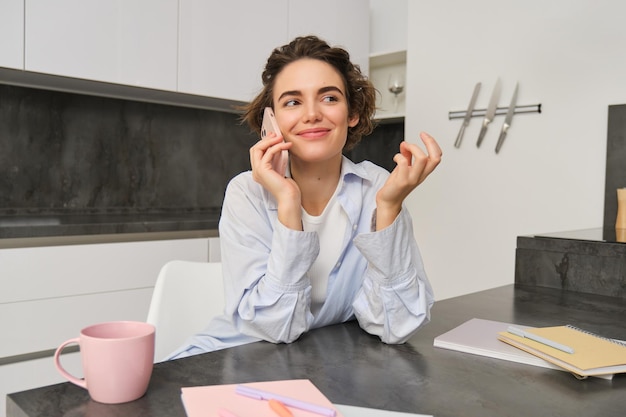 Portrait of beautiful girl talks on mobile phone has conversation answer a call in kitchen