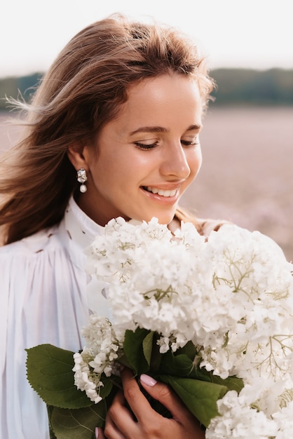 Ritratto di una bella ragazza in un abito bianco con un mazzo di fiori in un campo in estate