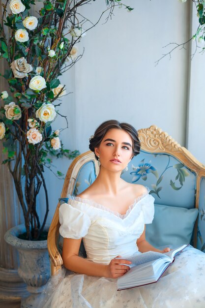 portrait of a beautiful girl who reads a book on a sofa in a beautiful dress