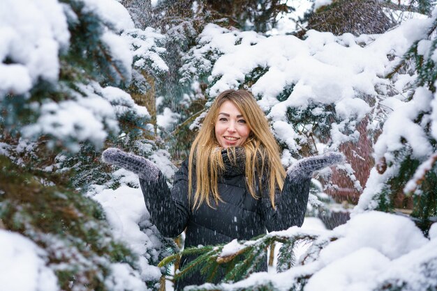 Portrait beautiful girl in winter snowy day near fir tree in forest young smiling woman playing with...