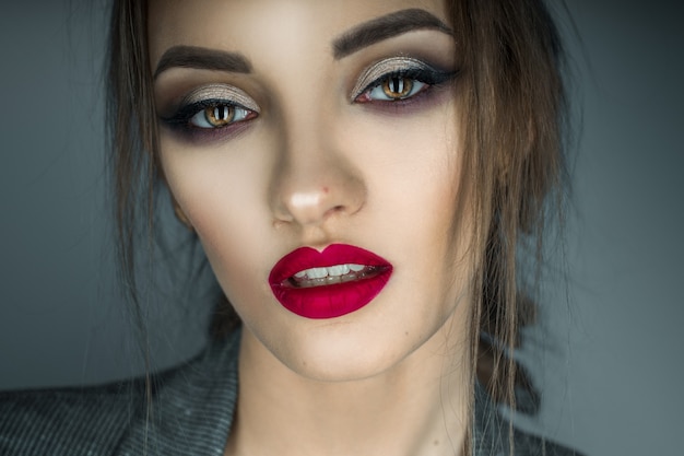 Ritratto di bella ragazza con gli occhi marroni e le labbra rosse che esaminano la macchina fotografica in studio