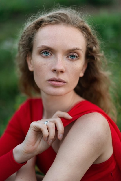 Portrait of a beautiful girl with curly hair and freckles on green grass in nature