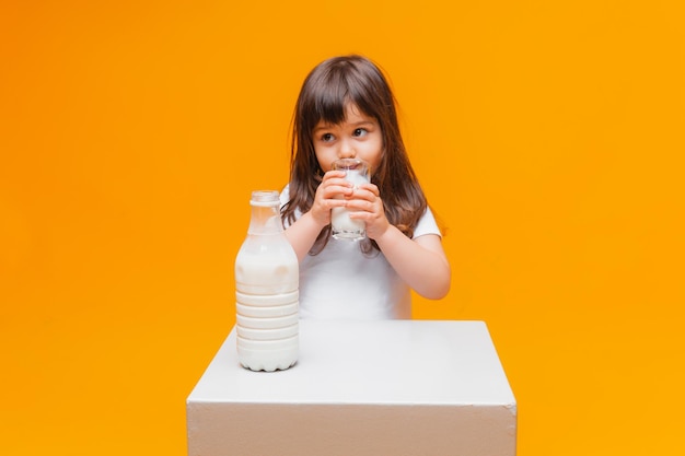 Portrait of beautiful girl with glass of milk on yellow background