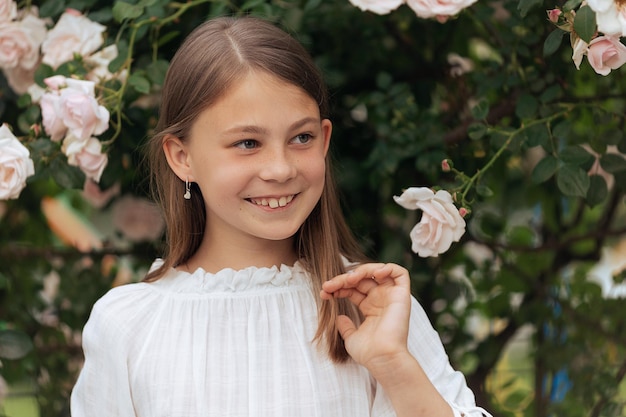 Portrait of a beautiful girl with long hair and freckles outside in the summer near roses