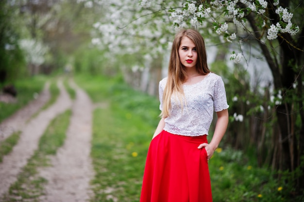 Portrait of beautiful girl with red lips at spring blossom garden, wear on red dress and white blouse.