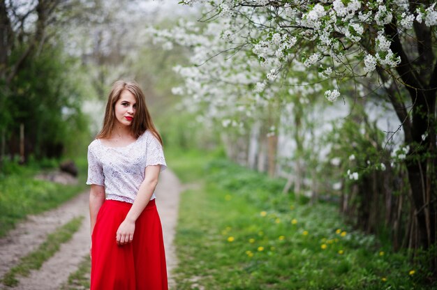 Portrait of beautiful girl with red lips at spring blossom garden, wear on red dress and white blouse