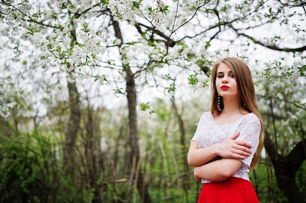 Ritratto di una bella ragazza con le labbra rosse al giardino di fiori di primavera, indossare abito rosso e camicetta bianca