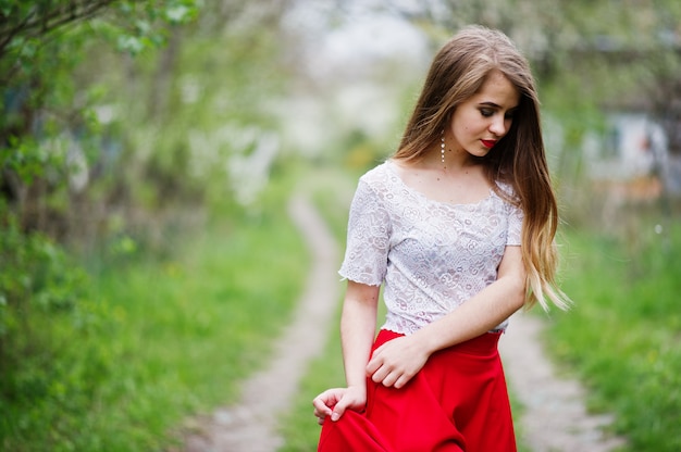 Portrait of beautiful girl with red lips at spring blossom garden, wear on red dress and white blouse