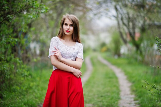 Portrait of beautiful girl with red lips at spring blossom garden, wear on red dress and white blouse