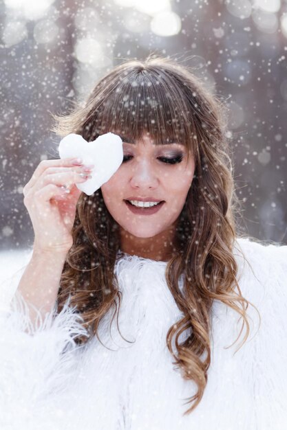 Foto ritratto di una bella ragazza con un cuore innevato nelle mani all'aperto