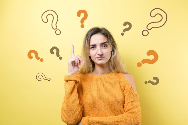 Portrait of a beautiful girl on a yellow background with question marks