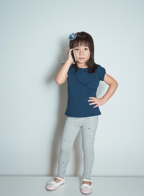 Portrait of a beautiful and happy asian little girl making a call on plain background