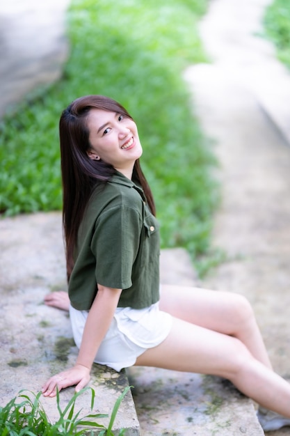 A portrait of beautiful happy asian woman traveler wearing brownish green dress stylish hipster Summer sunny lifestyle on the street outdoors at sunny summer day in park background