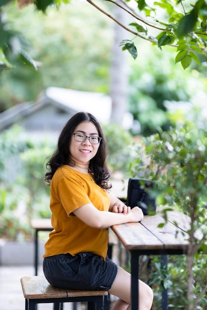 A portrait of beautiful happy asian woman traveler wearing yellow orange dress stylish hipster lifestyle on the street outdoors at summer day in park or in sitting coffee shop background