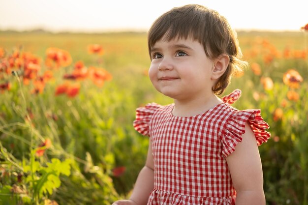 portrait beautiful happy baby girl in red dress smiling on field of poppies at summer sunset