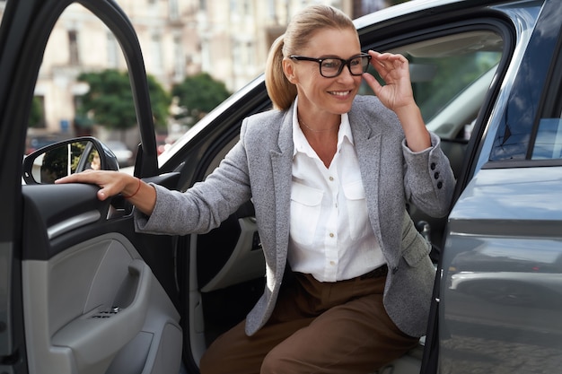 Ritratto di una bella e felice donna d'affari con gli occhiali che esce dalla sua auto moderna