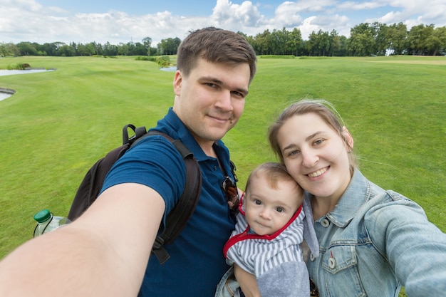 Photo portrait of beautiful happy family with baby boy making selfie at park