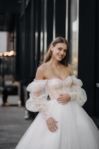 Portrait of beautiful happy girl with long hair in white wedding dress on the city background