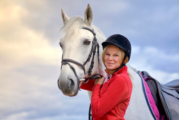 Portrait of a beautiful happy girl young woman rider equestrian smiling standing near white horse in