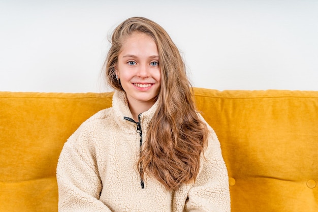 Portrait of a beautiful happy little teenage girl on a yellow sofa