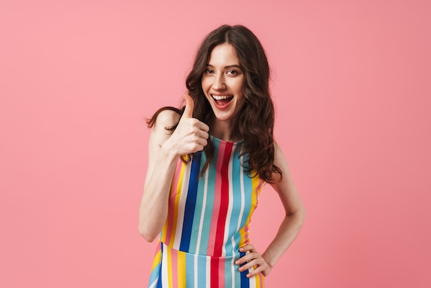 Portrait of beautiful happy positive cute woman posing isolated over pink wall showing thumbs up