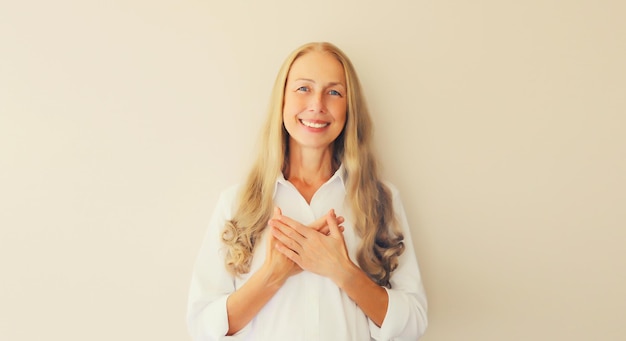 Portrait of beautiful happy smiling caucasian middle aged woman put folded hands on her heart