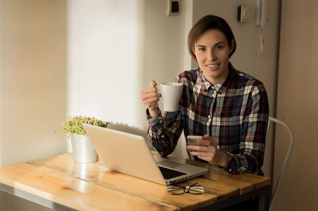 Portrait of beautiful happy smiling designer woman sitting at home office desk with cup of coffee