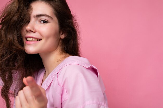 Portrait of beautiful happy smiling positive young curly brunette woman wearing pink shirt and grey