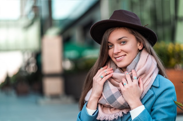 Portrait of beautiful happy smiling stylish trendy brunette hipster woman in a brown hat with cozy warm scarf in the city