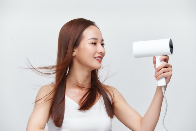 Portrait of beautiful happy woman drying her long hair with dryer over white background