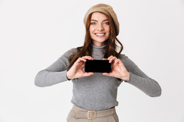 Portrait of beautiful happy woman isolated on white wall showing display of mobile phone.