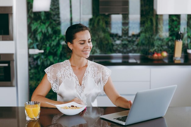 The portrait of beautiful happy woman working with laptop while breakfast with cereals and milk