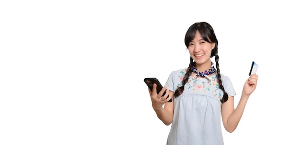 Портрет красивой счастливой молодой азиатки в джинсовом платье с кредитной картой и смартфоном на белом фоне