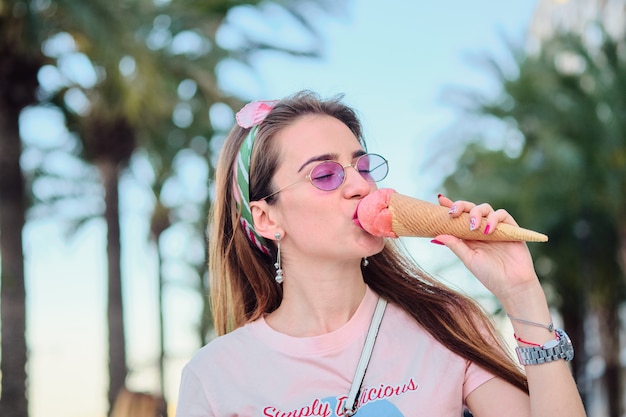 Portrait of beautiful happy young woman in pink sunglasses eating pink ice cream.