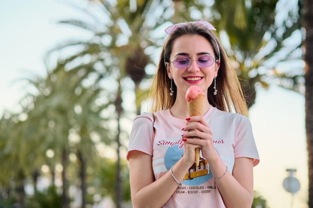 Photo portrait of beautiful happy young woman in pink sunglasses eating pink ice cream.