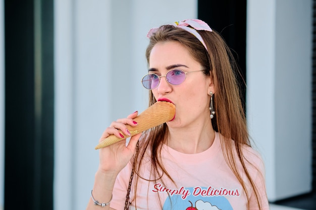 Portrait of beautiful happy young woman in pink sunglasses eating pink ice cream.