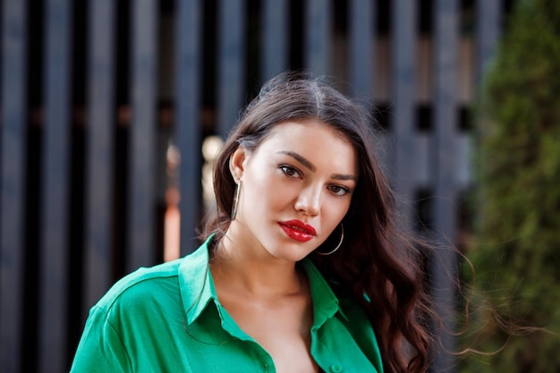 Ritratto di bella donna ispanica in camicia verde davanti all'edificio urbano della parete nera dello scaffale