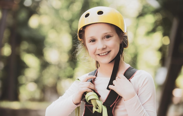 Portrait of a beautiful kid on a rope park among trees happy little girl climbing a tree helmet safe
