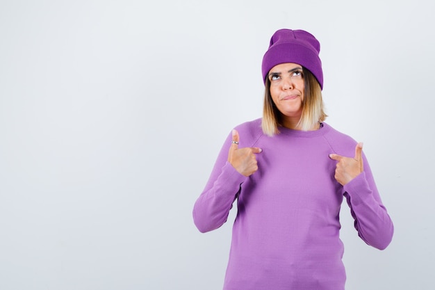 Photo portrait of beautiful lady pointing at herself in sweater, beanie and looking confident front view