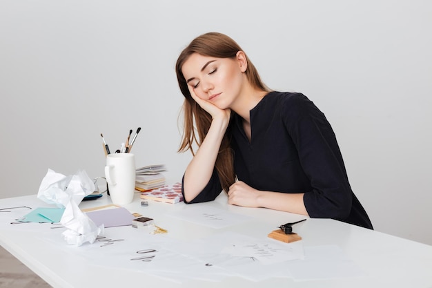 Portrait of beautiful lady sitting at the white desk and sleeping while leaning head on her hand isolated