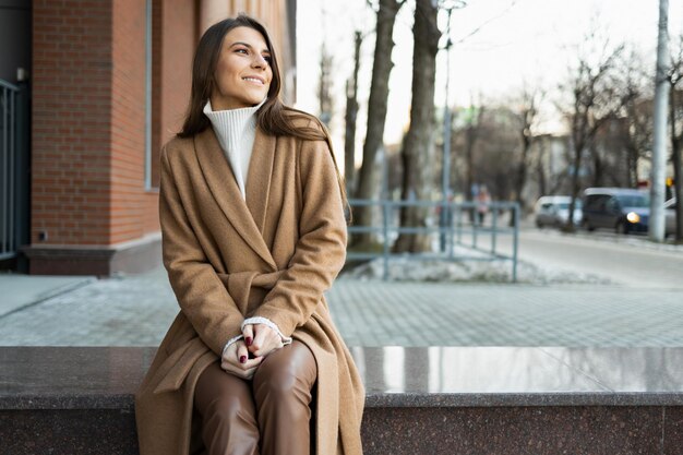 Portrait of beautiful lady in stylish clothes sitting on the street