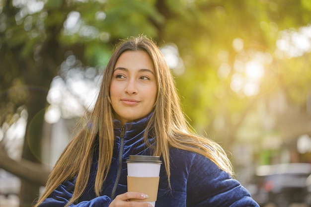 Portrait of beautiful latin girl drinking coffee on a public park bench with copy space