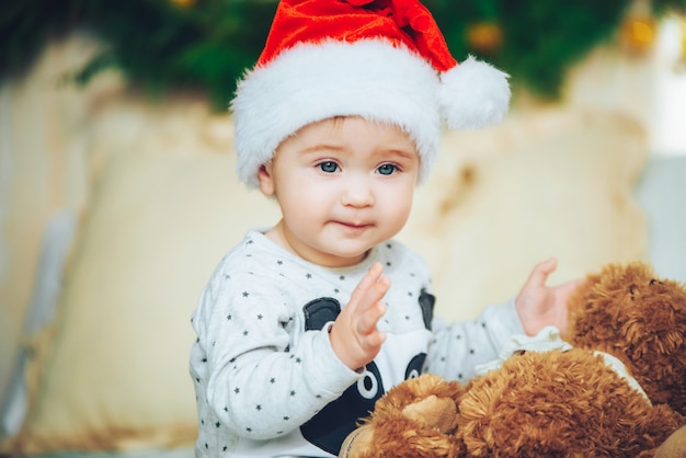 Portrait of beautiful little baby boy celebrates Christmas. New Year's holidays. Adorable funny child in Santa red hat with Christmas gift. Christmas concept.