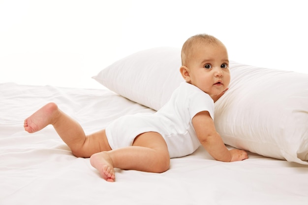 Portrait of beautiful little baby girl toddler in onesie posing on bed against white background