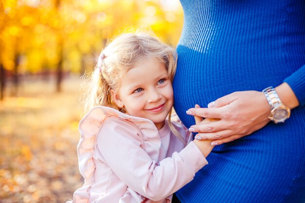 Portrait of beautiful little girl holding her pregnant mother's belly