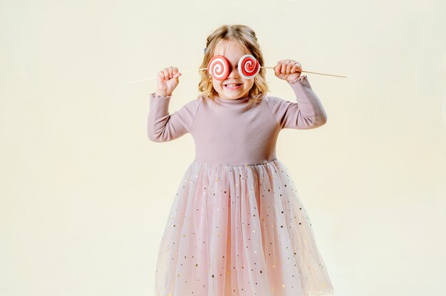 Portrait of a beautiful little girl on a light background with a lollipop in hand. Food concept