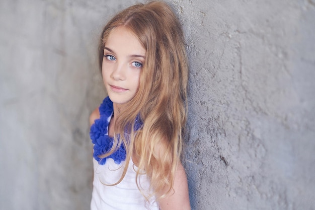 Portrait of a beautiful little girl model posing while leaning against a wall in a studio.