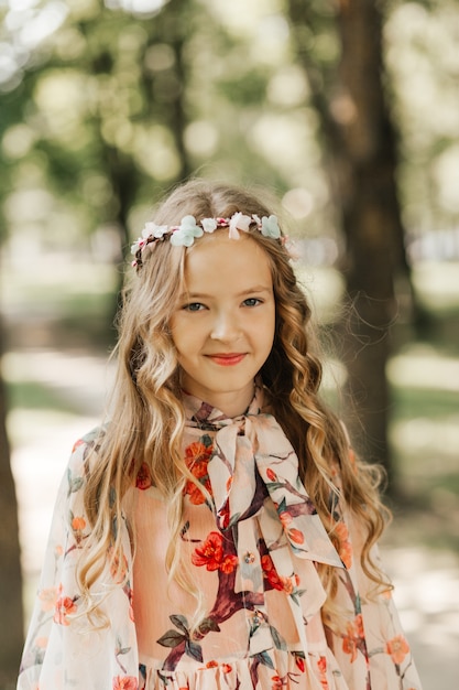 Portrait of a beautiful little girl with long blonde hair in the park in the summer