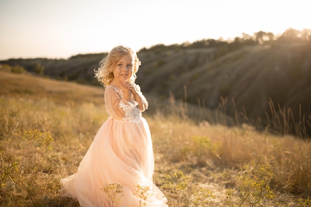 Portrait of a beautiful little princess girl in a pink dress. Posing in a field at sunset